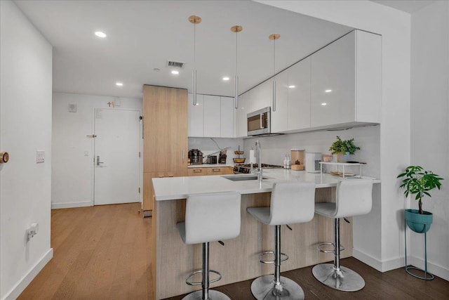 131-05 40th Rd Unit 15G, Flushing, NY 11354 - kitchen with stainless steel microwave, modern cabinets, a peninsula, light wood-style flooring, and a kitchen breakfast bar