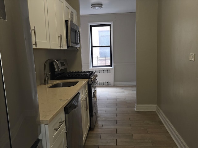 55 E 190th St Unit 45, Bronx, NY 10468 - kitchen featuring radiator, stainless steel appliances, white cabinetry, light stone counters, and wood finished floors