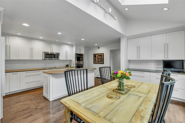 74 Woods Dr, Roslyn, NY 11576 - kitchen with stainless steel appliances, a kitchen island with sink, recessed lighting, white cabinets, and vaulted ceiling