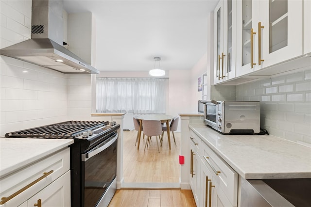 102-30 66th Rd Unit 1G, Forest Hills, NY 11375 - kitchen featuring gas range, wall chimney exhaust hood, backsplash, white cabinetry, and light stone counters