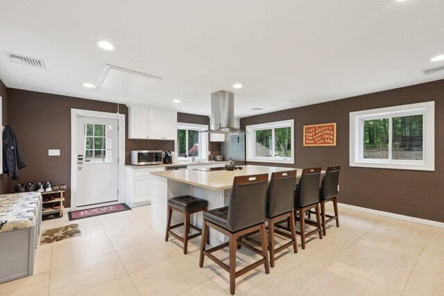 160 S Mountain Rd, New City, NY 10956 - kitchen featuring island range hood, stainless steel microwave, light countertops, white cabinets, and a kitchen bar
