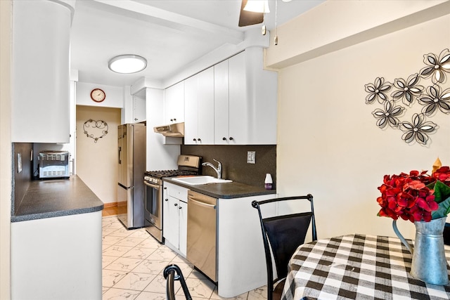 151-25 88th St Unit 1D, Howard Beach, NY 11414 - kitchen featuring stainless steel appliances, under cabinet range hood, dark countertops, white cabinetry, and light marble finish floors