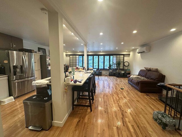 2936 216th St, Bayside, NY 11360 - kitchen with stainless steel refrigerator with ice dispenser, a wall unit AC, open floor plan, light wood-style flooring, and recessed lighting