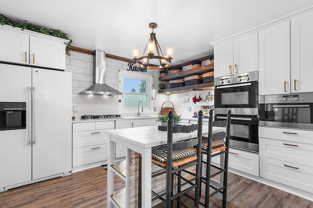 121 Thomas Ave, Bethpage, NY 11714 - kitchen with appliances with stainless steel finishes, wall chimney exhaust hood, a chandelier, backsplash, and dark wood-style floors