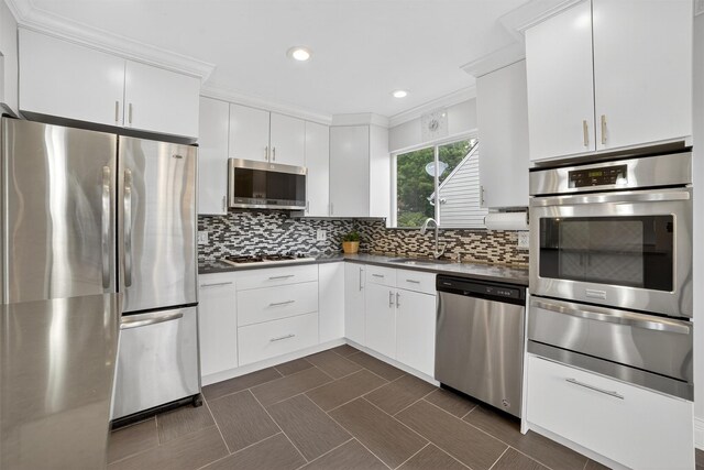 7 Fuller Rd, Ossining, NY 10562 - kitchen featuring appliances with stainless steel finishes, a warming drawer, dark countertops, white cabinetry, and crown molding