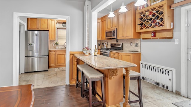17111 Bagley Ave, Flushing, NY 11358 - kitchen featuring appliances with stainless steel finishes, radiator, decorative backsplash, a kitchen bar, and light stone countertops