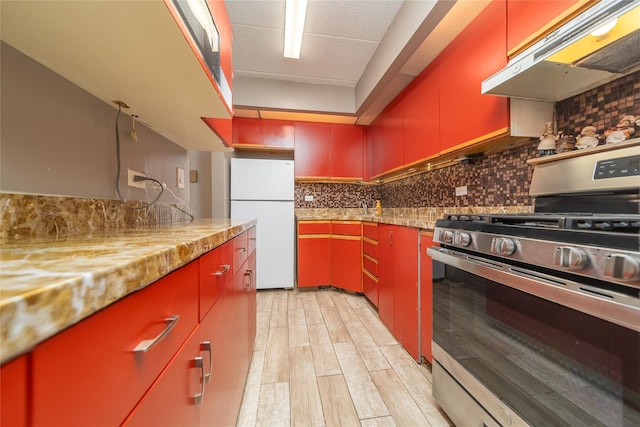92-29 Queens Blvd Unit 14B, Rego Park, NY 11374 - kitchen with gas range, red cabinetry, freestanding refrigerator, under cabinet range hood, and decorative backsplash
