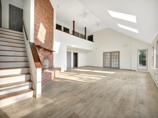 285 Hill Rd, Goshen, NY 10940 - unfurnished living room featuring high vaulted ceiling, a brick fireplace, a skylight, stairs, and light wood finished floors