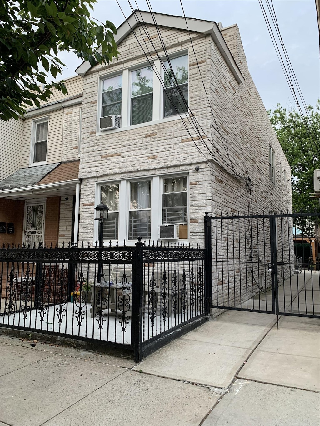 9721 83rd St, Ozone Park, NY 11416 - view of front of home with stone siding, a fenced front yard, a gate, and cooling unit