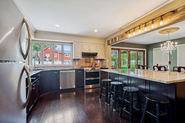 17 Sterling Dr, Lake Grove, NY 11755 - kitchen featuring appliances with stainless steel finishes, under cabinet range hood, a breakfast bar area, dark wood finished floors, and ornamental molding