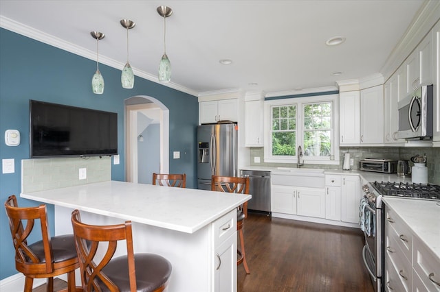 3665 Lufberry Ave, Wantagh, NY 11793 - kitchen featuring appliances with stainless steel finishes, a kitchen breakfast bar, arched walkways, tasteful backsplash, and white cabinetry