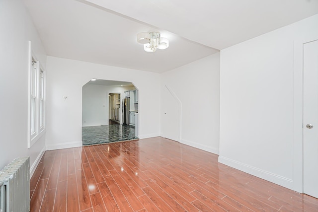 592 E 39th St, Brooklyn, NY 11203 - spare room with radiator heating unit, arched walkways, wood finished floors, and a chandelier