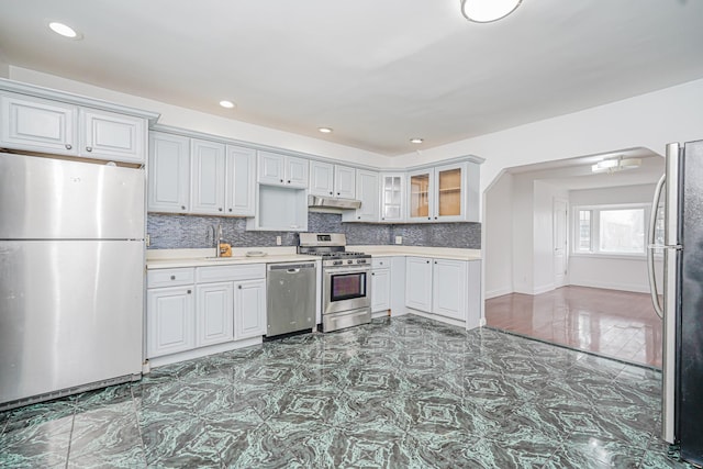592 E 39th St, Brooklyn, NY 11203 - kitchen with appliances with stainless steel finishes, light countertops, under cabinet range hood, tasteful backsplash, and glass insert cabinets
