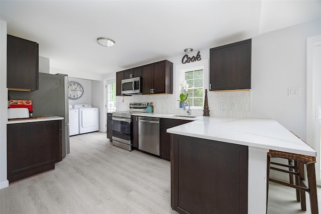 47 Clay Hill Rd, Tivoli, NY 12583 - kitchen with washing machine and clothes dryer, appliances with stainless steel finishes, a peninsula, dark brown cabinetry, and light wood-style floors