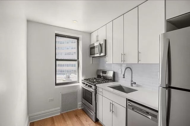 97-25 64th Ave Unit 5D, Rego Park, NY 11374 - kitchen featuring stainless steel appliances, light countertops, white cabinetry, tasteful backsplash, and light wood-type flooring