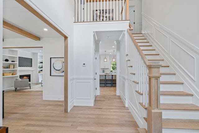 30 Middleville Rd, Northport, NY 11768 - staircase with a decorative wall, wood finished floors, a lit fireplace, beam ceiling, and wainscoting