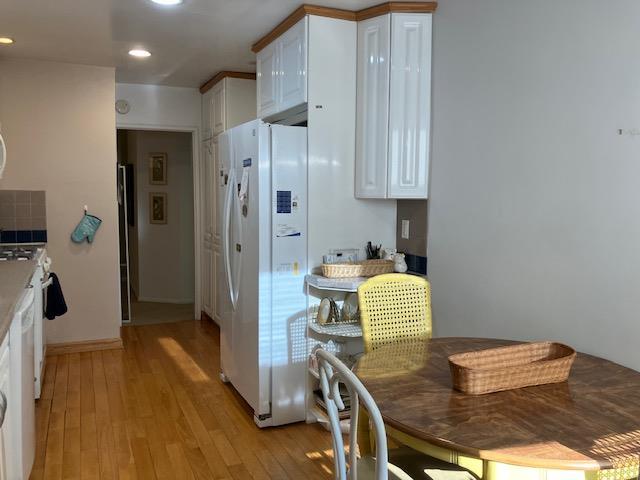 20 Chapel Pl Unit 1H, Great Neck, NY 11021 - kitchen featuring white fridge with ice dispenser, white cabinetry, light wood-style floors, recessed lighting, and range