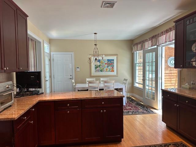 1 Sunset Ave, East Quogue, NY 11942 - kitchen featuring a peninsula, light wood-type flooring, light stone countertops, a chandelier, and glass insert cabinets