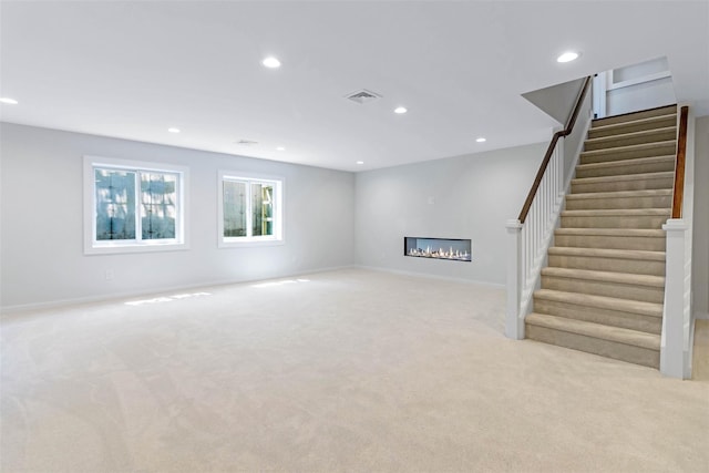 130 Sunset Ln, Greenport, NY 11944 - unfurnished living room with a glass covered fireplace, recessed lighting, light colored carpet, and stairs