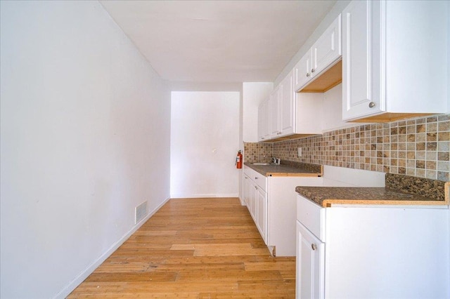 221 E Main St, Middletown, NY 10940 - kitchen featuring backsplash, light wood finished floors, white cabinetry, and dark countertops