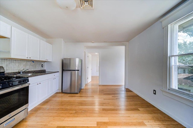 221 E Main St, Middletown, NY 10940 - kitchen with stainless steel appliances, white cabinets, light wood-type flooring, backsplash, and dark countertops