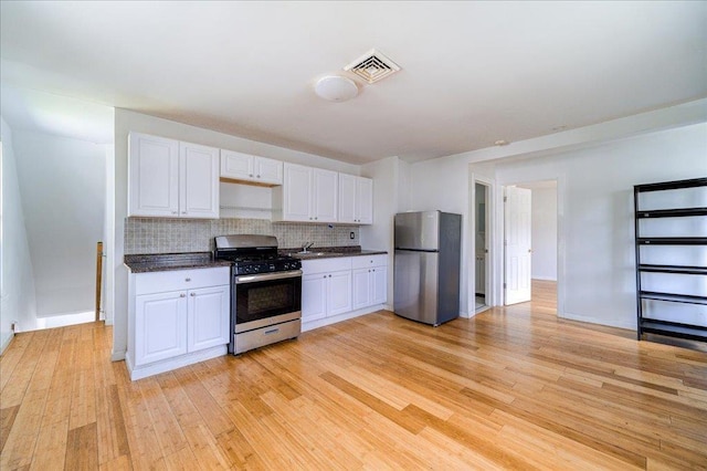 221 E Main St, Middletown, NY 10940 - kitchen with appliances with stainless steel finishes, light wood-style floors, white cabinets, decorative backsplash, and dark countertops