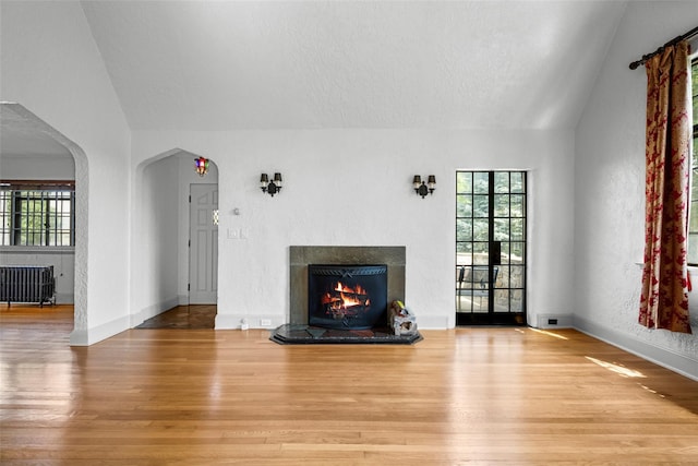 1 Highwood Way, Larchmont, NY 10538 - unfurnished living room featuring radiator heating unit, wood finished floors, lofted ceiling, a lit fireplace, and a textured ceiling