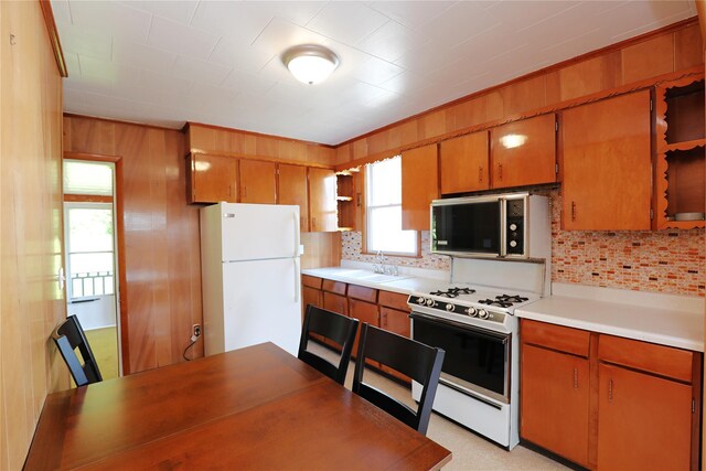 144 Hudson St, Saugerties, NY 12477 - kitchen with white appliances, decorative backsplash, brown cabinetry, light countertops, and wooden walls