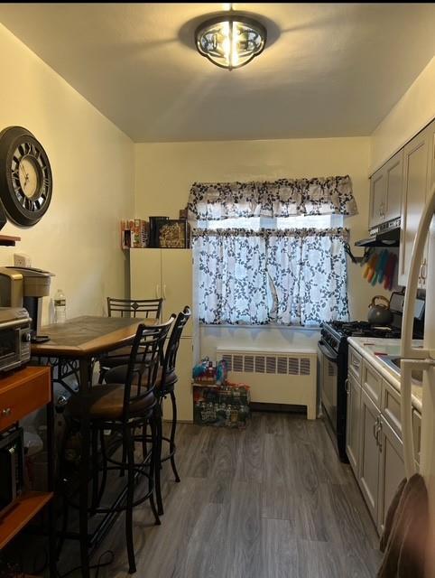 6404 78th St, Middle Village, NY 11379 - kitchen with radiator heating unit, gas stove, dark wood finished floors, under cabinet range hood, and light countertops