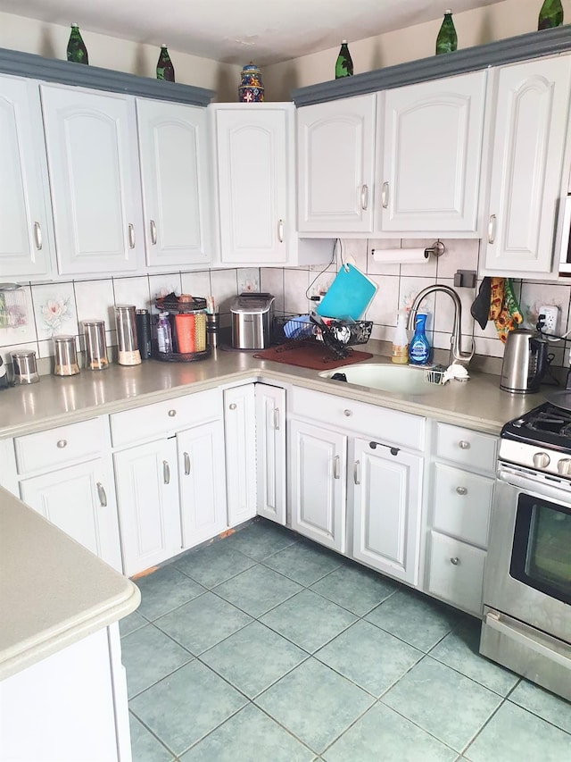 12826 Gotham Rd, South Ozone Park, NY 11420 - kitchen featuring stainless steel range with gas stovetop, light countertops, decorative backsplash, and white cabinets