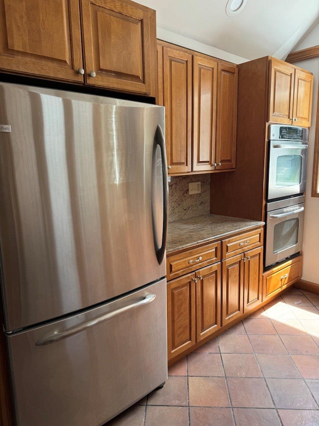 390 Atlantic Ave, East Rockaway, NY 11518 - kitchen featuring appliances with stainless steel finishes, light tile patterned floors, brown cabinetry, and decorative backsplash