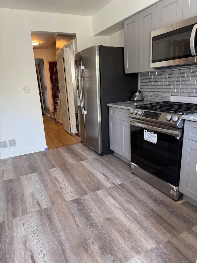 1319 Hicks St, Bronx, NY 10469 - kitchen with stainless steel appliances, gray cabinetry, light wood-style flooring, and decorative backsplash