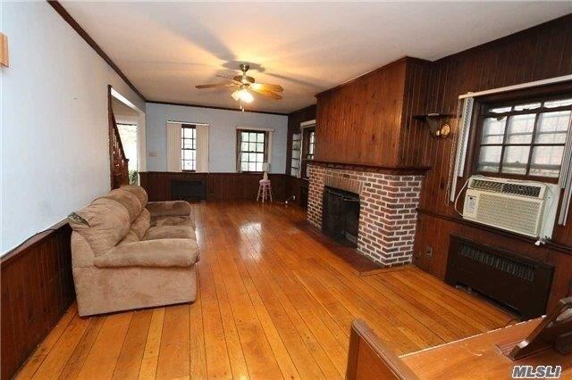 85-24 Eton St, Jamaica Estates, NY 11432 - living room featuring a brick fireplace, wooden walls, ceiling fan, light wood-type flooring, and cooling unit