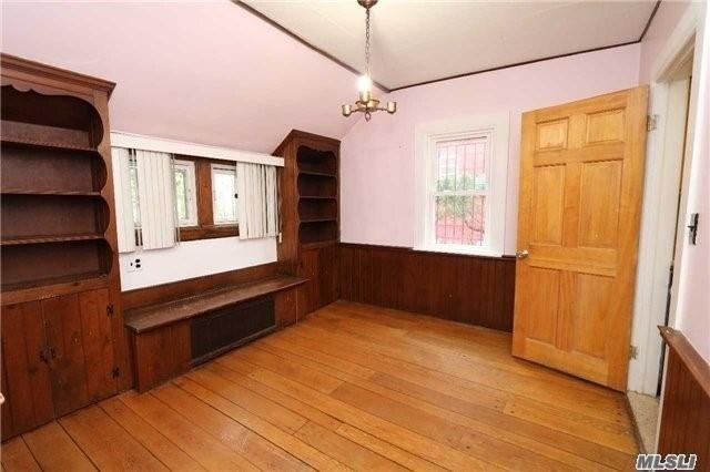 85-24 Eton St, Jamaica Estates, NY 11432 - unfurnished dining area featuring lofted ceiling, light wood-type flooring, a chandelier, wainscoting, and wooden walls