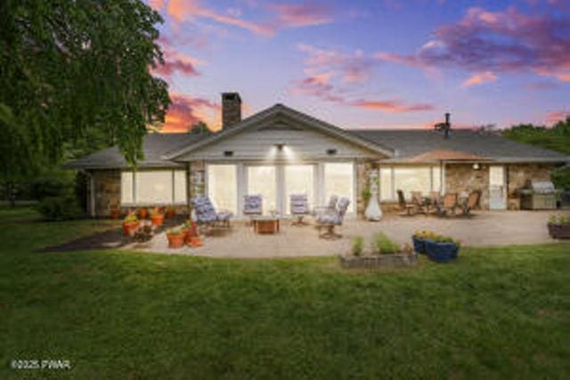 312 E Ann St, Milford, PA 18337 - back of house at dusk with a patio area, a chimney, a yard, and stone siding