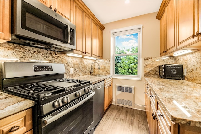 609 NE Palmer Rd Unit 4J, Yonkers, NY 10701 - kitchen featuring stainless steel appliances, radiator heating unit, light wood-style floors, light stone counters, and tasteful backsplash