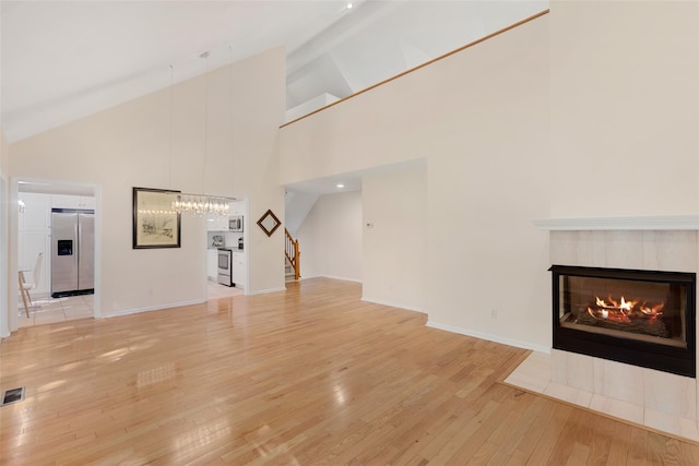 15 Deertree Ln, Briarcliff Manor, NY 10510 - unfurnished living room with light wood-type flooring, stairs, high vaulted ceiling, a tile fireplace, and a chandelier