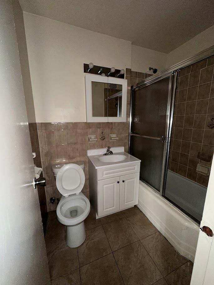 2385 Barker Ave Unit 6B, Bronx, NY 10467 - full bathroom featuring tile walls, tile patterned flooring, vanity, combined bath / shower with glass door, and wainscoting