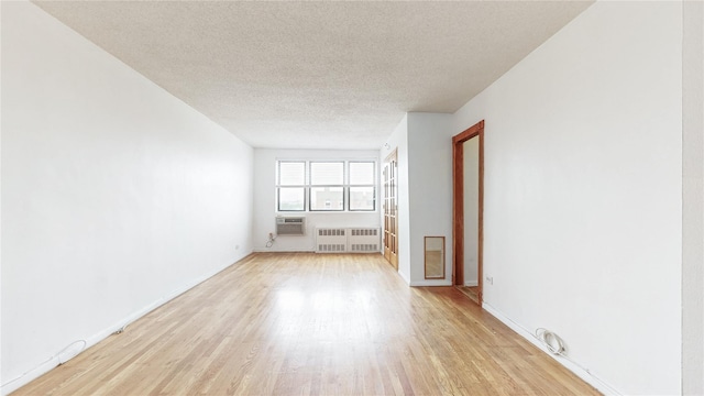 8420 153rd Ave Unit 6H, Howard Beach, NY 11414 - empty room featuring light wood-type flooring, a textured ceiling, a wall unit AC, and radiator