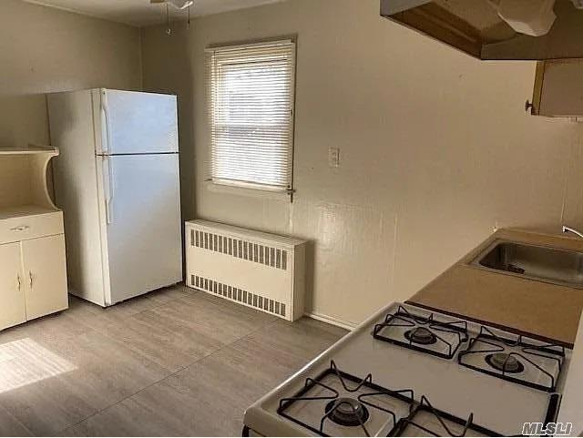 116-46 171st St, Jamaica, NY 11434 - kitchen with radiator, white appliances, extractor fan, and white cabinets