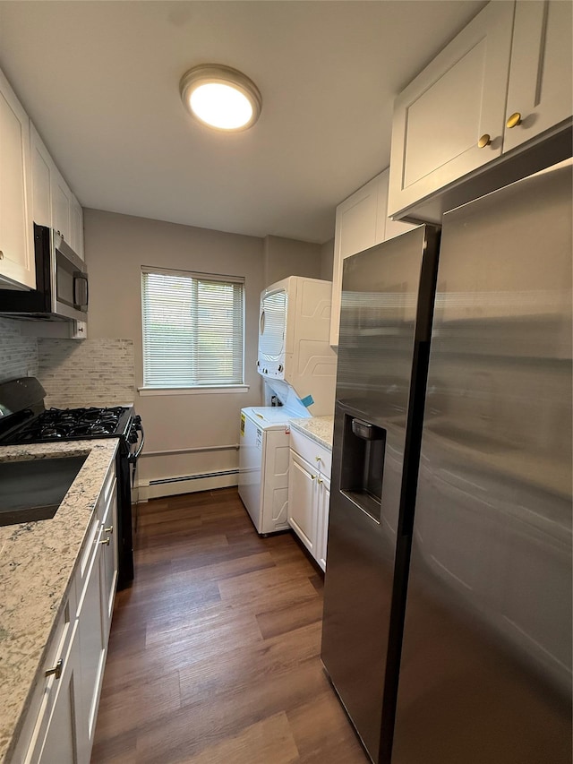 77 Adams Rd Unit 1D, Central Islip, NY 11722 - kitchen featuring stainless steel appliances, estacked washer and dryer, white cabinets, light stone counters, and dark wood-style floors