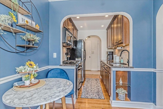 104 S Village Ave S Unit 1F, Rockville Centre, NY 11570 - kitchen with arched walkways, stainless steel appliances, light wood-type flooring, dark stone counters, and brown cabinetry