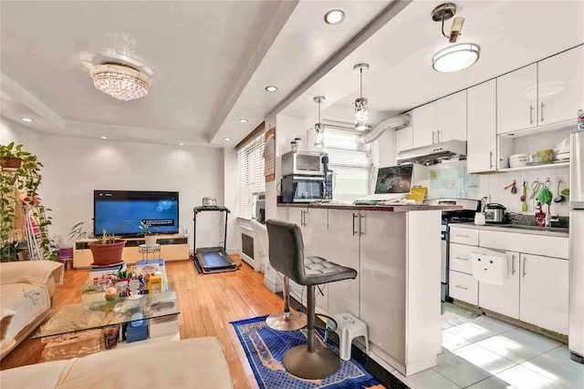 141-15 28th Ave Unit 1G, Flushing, NY 11354 - kitchen with stainless steel gas range, under cabinet range hood, open floor plan, a breakfast bar, and white cabinetry