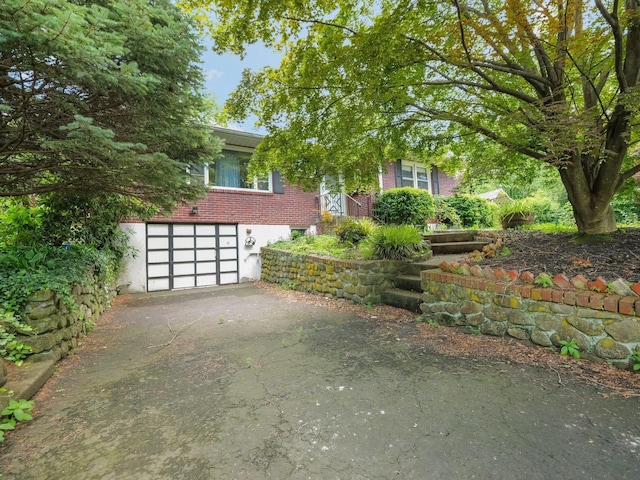 19 E Orchard St, Nanuet, NY 10954 - view of property hidden behind natural elements featuring brick siding, driveway, and an attached garage