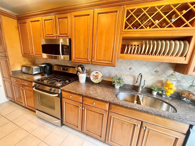 7863 79th Ln, Glendale, NY 11385 - kitchen with appliances with stainless steel finishes, light tile patterned floors, brown cabinetry, decorative backsplash, and dark stone counters