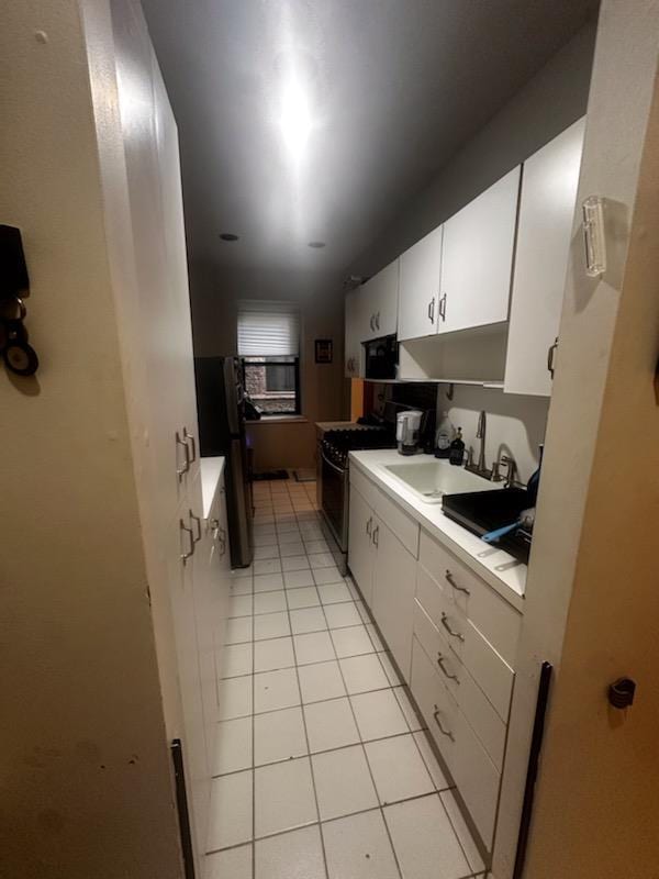 141 Wyckoff Pl Unit 1F, Woodmere, NY 11598 - kitchen featuring range with gas stovetop, light tile patterned flooring, light countertops, freestanding refrigerator, and white cabinets
