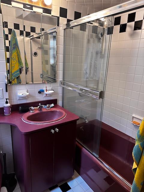141 Wyckoff Pl Unit 1F, Woodmere, NY 11598 - bathroom featuring tile walls, shower / bath combination with glass door, vanity, tile patterned flooring, and backsplash