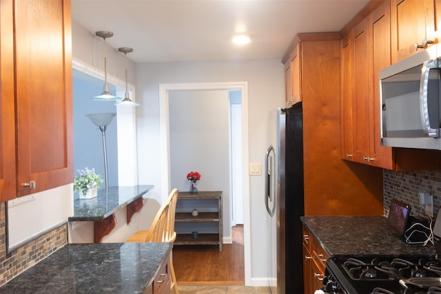 95 N Broadway Unit D2-5, White Plains, NY 10603 - kitchen featuring stainless steel appliances, dark stone counters, decorative backsplash, brown cabinetry, and decorative light fixtures
