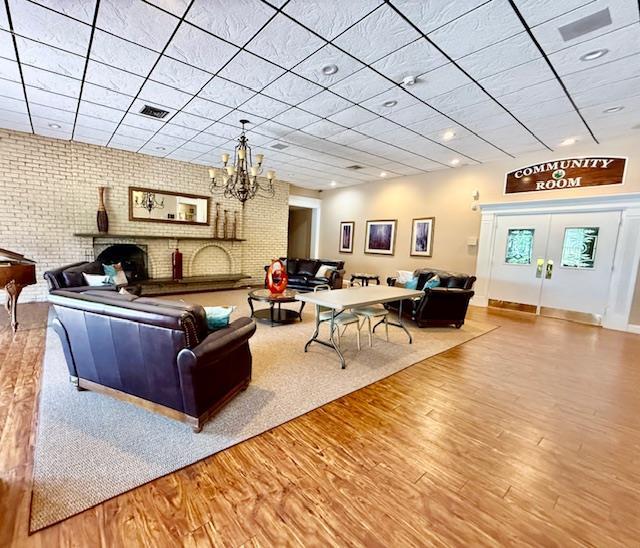 1104 Drew Dr, Saint James, NY 11780 - living room with a paneled ceiling, wood finished floors, brick wall, a chandelier, and a fireplace