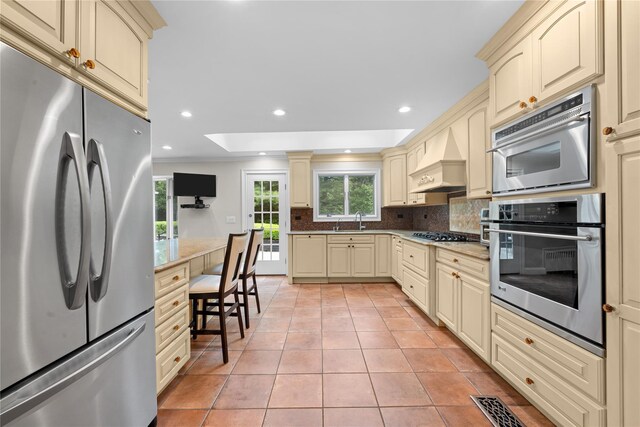 156 Lefferts Rd, Woodmere, NY 11598 - kitchen featuring stainless steel appliances, cream cabinetry, backsplash, light tile patterned flooring, and custom exhaust hood